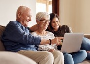 Granddaughter looking at laptop computer on couch with grandparents